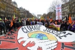 muitas pessoas em evento na rua apresentam uma enorme faixa escrito justiça Climática em inglês e protesta sobre a injustiça.